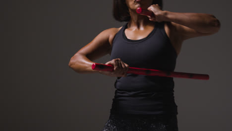 Close-Up-Studio-Shot-Of-Mature-Woman-Wearing-Gym-Fitness-Clothing-Exercising-With-Martial-Arts-Escrima-Sticks